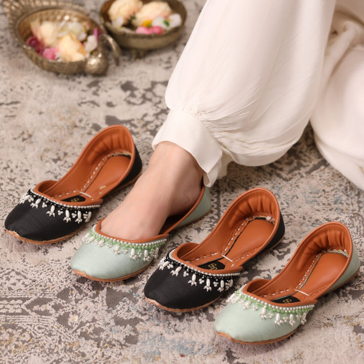 Pair of black and light green flat khussas with decorative elements on a textured surface.