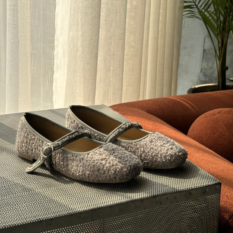 Pair of gray textured mary janes shoes on a textured surface with a blurred indoor background