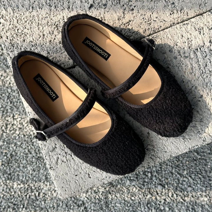 Pair of black shoes mary janes with a brand label on a concrete surface