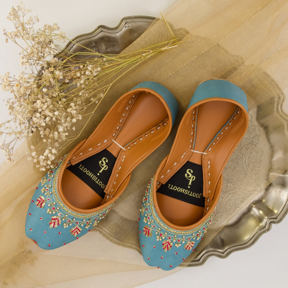 Pair of blue embroidered khussas on a decorative tray with a light background