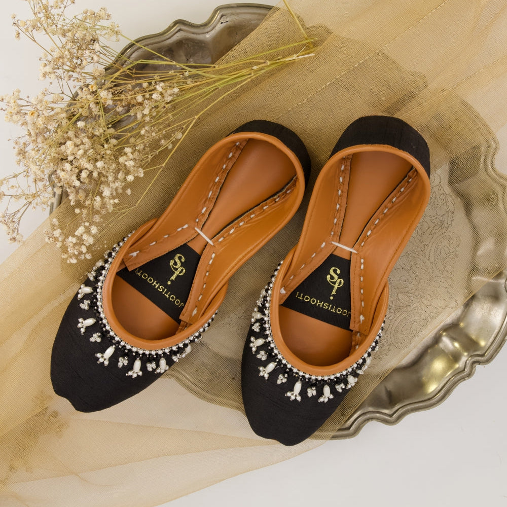 Black and brown khussas with decorative elements on a decorative tray with flowers.